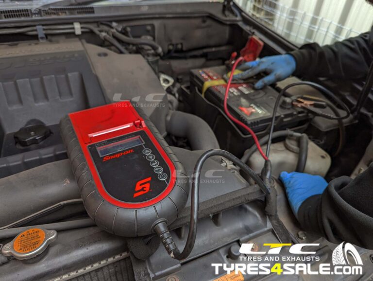 Technician testing a car battery with a digital tester in the engine bay